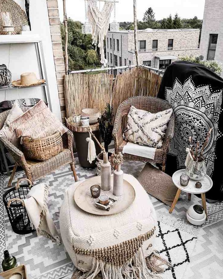 a black and white boho balcony with wicker chairs, a Moroccan pouf, a small side table, baskets and candle lanterns and beautiful Morocco-inspired blankets, pillows and rugs