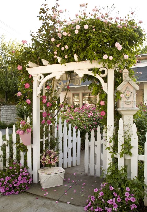 pink, blush and white blooming vines over the gate are amazing to make the entrance feel cottage-like, it's a bit messy and hot pink blooms at the gate feel as if it's a garden already