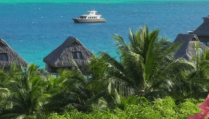 Turquoise and Blue Pacific Ocean with Boat in Background and Overwater Bungalows, Tropical Plants and Flowers in Foreground in Bora Bora French Polynesia