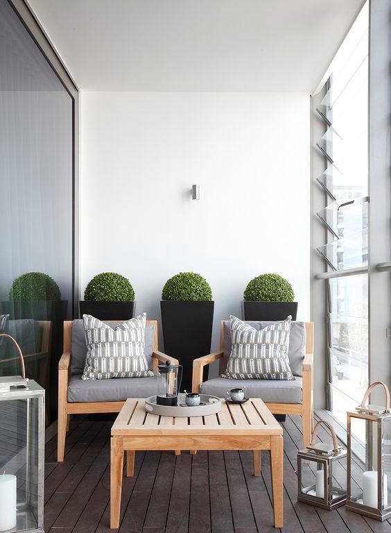 a stylish minimalist space with wooden furniture, candle lanterns and tall planters with greenery