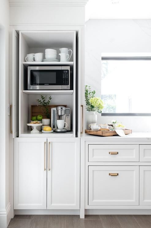 a small and narrow cabinet turned into a hidden tea or coffee bar, with appliances, mugs and a microwave too