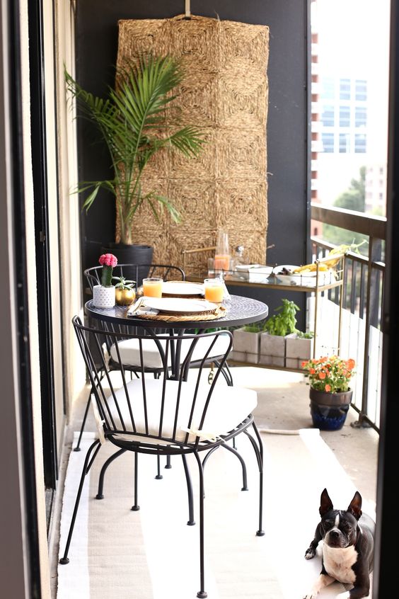 a round table, comfy forged chairs, a stand with plants and dishes on top, a jute hanging on the wall