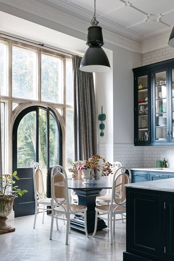 an elegant kitchen eat-in space right in the center, with a vintage dark wood table and airy rattan chairs