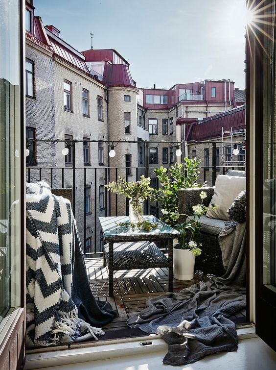 a dark wicker furniture set with potted greener, blankets and lights on the railing