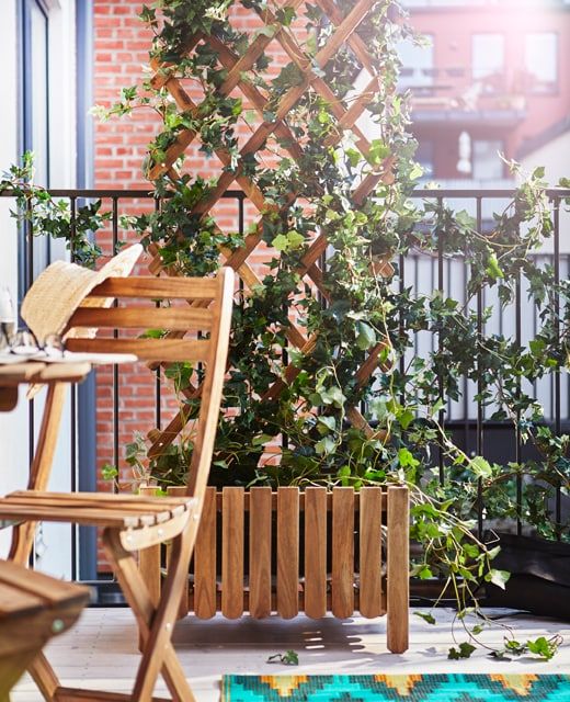 a balcony with a planter with a trellis and vines climbing up, folding furniture and a bold rug is cool and cozy