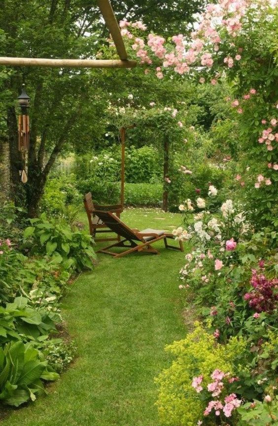 a beautiful and welcoming outdoor space with a green lawn, greenery and pink and white blooms plus some simple garden furniture