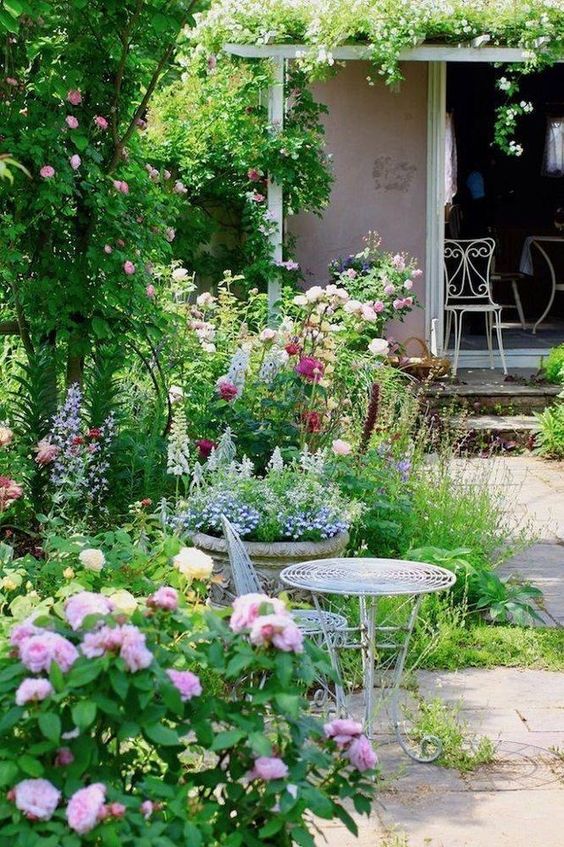 a beautiful blooming space with lots of greenery and some pastel flowers plus refined white garden furniture is amazing