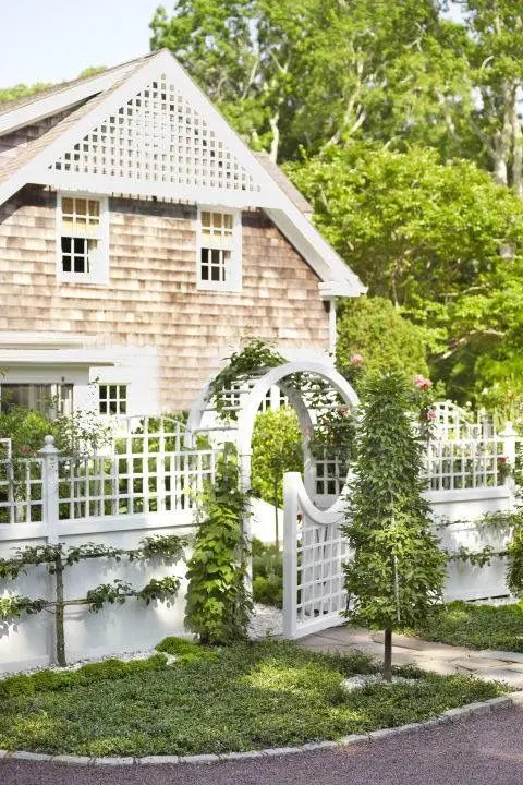a beautiful cottage white fence with a solid and lattice part, a gate with an arbor  and some green climbers to refresh the look