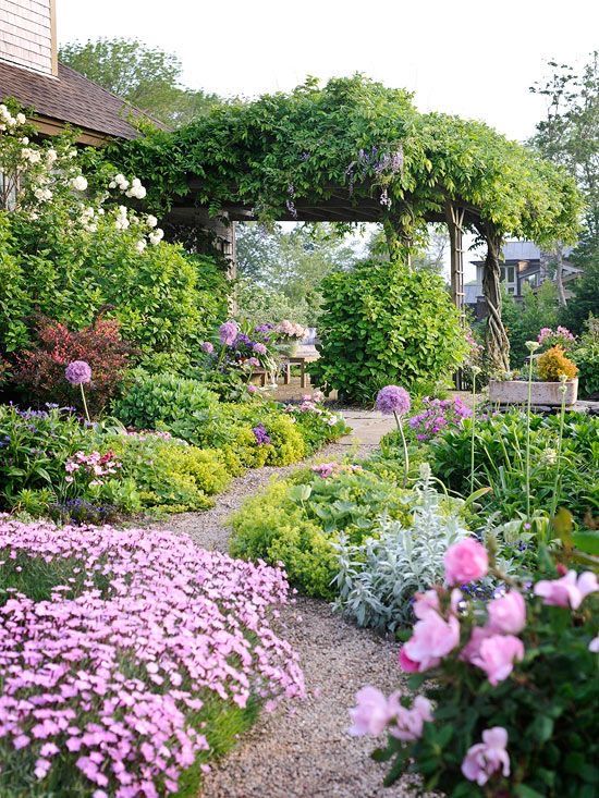 a beautiful garden with greenery and pink blooms and a gravel path is a stunning space that welcomes in