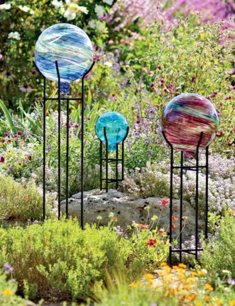 a beautiful garden with greenery, rocks, bright flowers, colorful gazing balls on stands that add even more color to the space