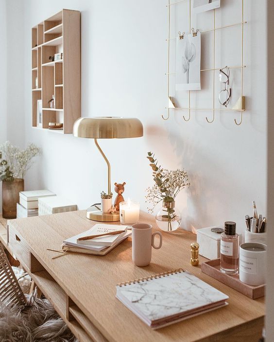 a beautiful neutral workspace with a desk with accessories and decor, a table lamp and greenery, a gold grid with various stuff and a chair