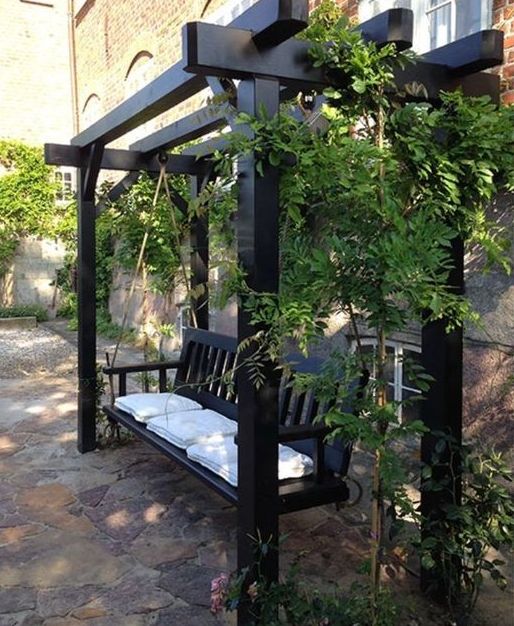 a black arbor frame with a hanging bench, white cushions, greenery on top is a stylish idea for a modern or Scandinavian space