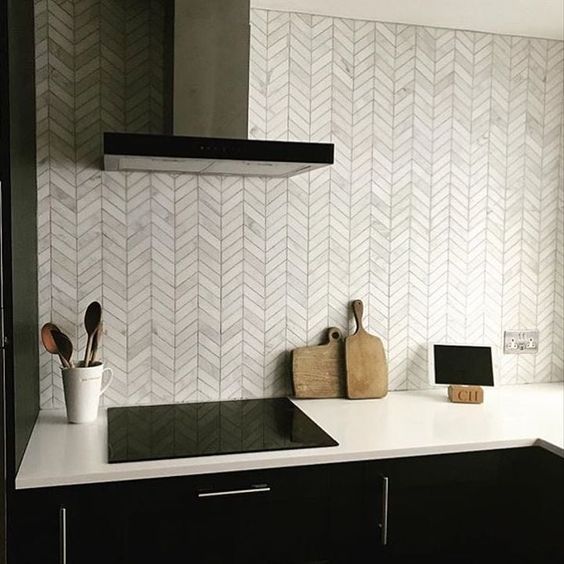 a black kitchen with a white marble chevron tile backsplash and black appliances is adorable and chic