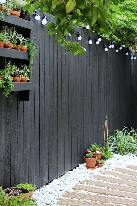 a black wooden fence with a black shelf with planters and lights is a nice solution for a Scandinavian space