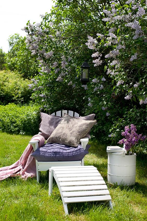 a blooming space with some bushes, a green lawn, a simple garden chair and a footrest is a lovely nook to enjoy the views