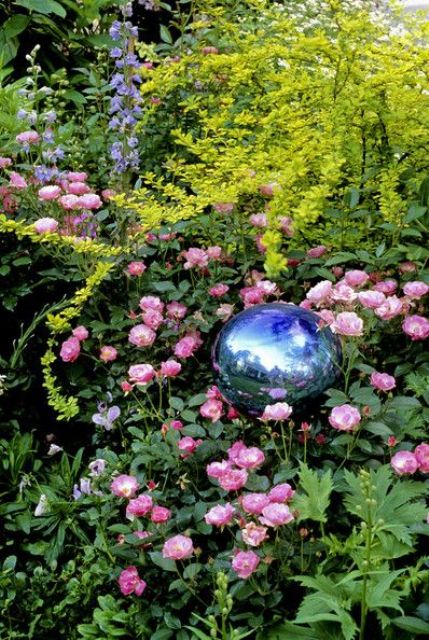 a blue gazing ball placed into pink roses adds color and interest to the garden bed and makes it unusual and bold