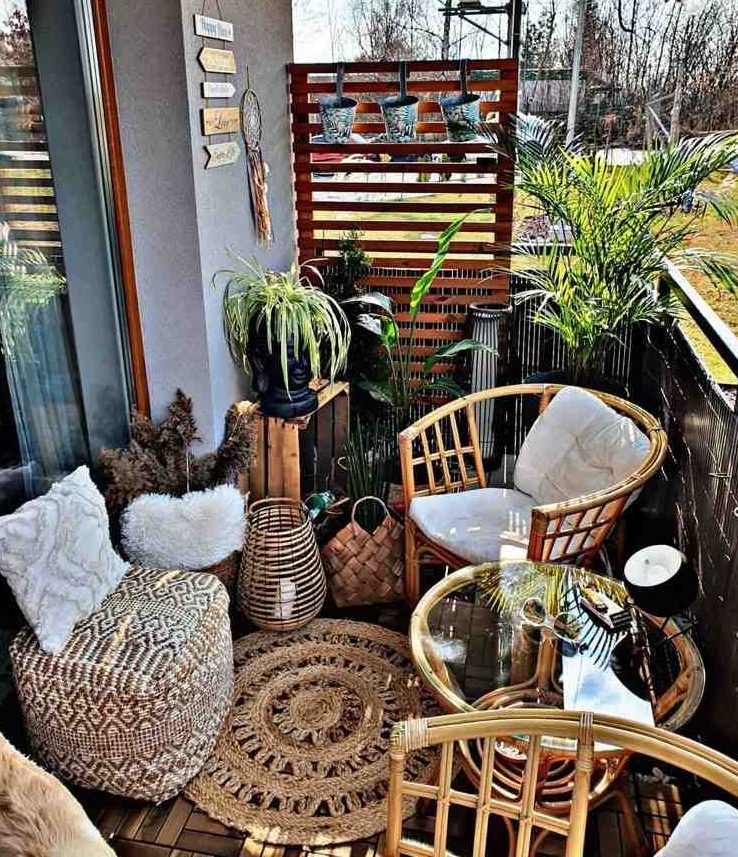 a boho balcony with rattan chairs and a table, a boho pouf and a pillow, a jute rug, potted greenery and candle lanterns is small but cool