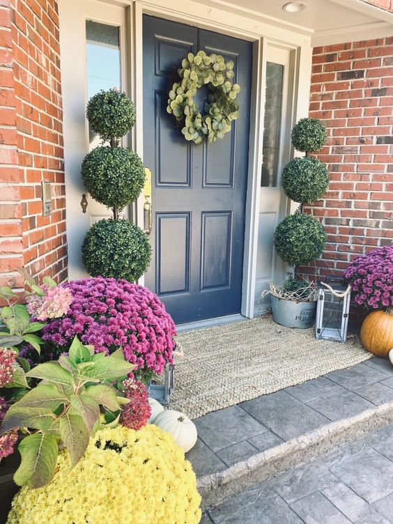 a bold farmhouse porch with tall topiaries, bold blooms in pots, pumpkins and leaves is amazing for the fall