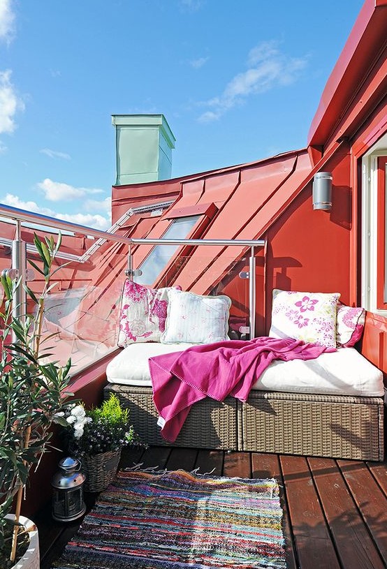 a bright balcony with an upholstered bench, a colorful rug and bright textiles, potted plants and blooms is fun