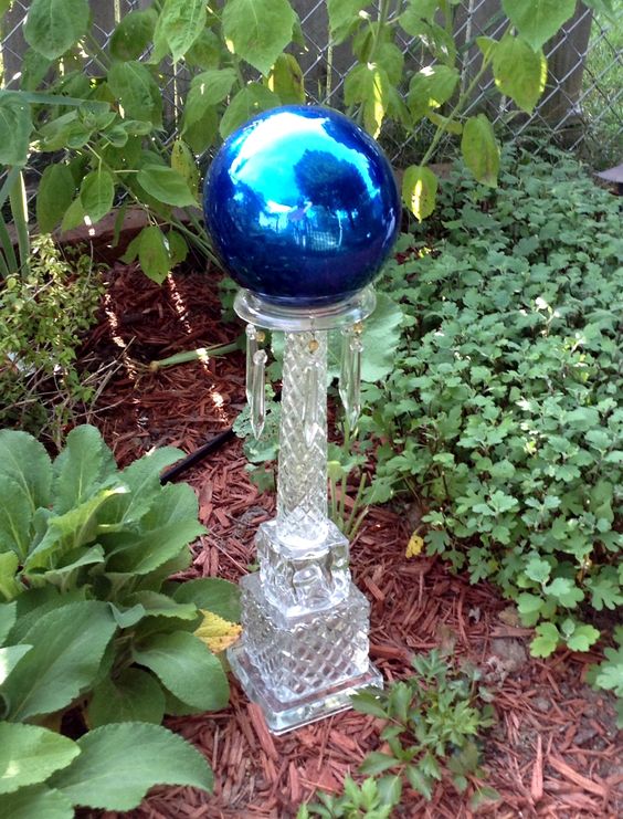 a bright blue gazing ball with a glossy finish placed on a glass stand with pendants is a cool decoration that looks unusual
