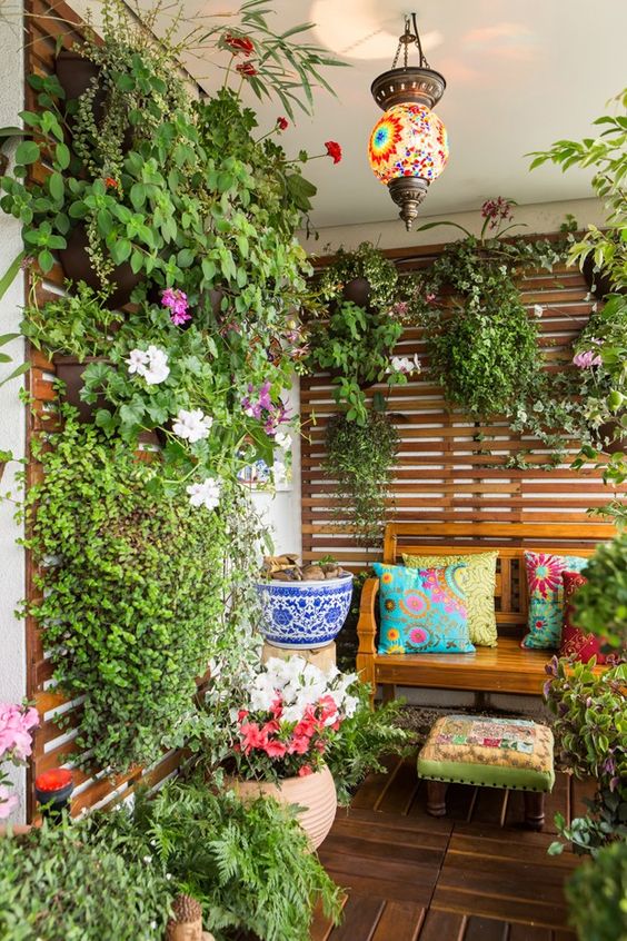 a bright boho balcony with a wooden bench, a trellis with greenery and blooms and another matching one, a colorful boho lamp