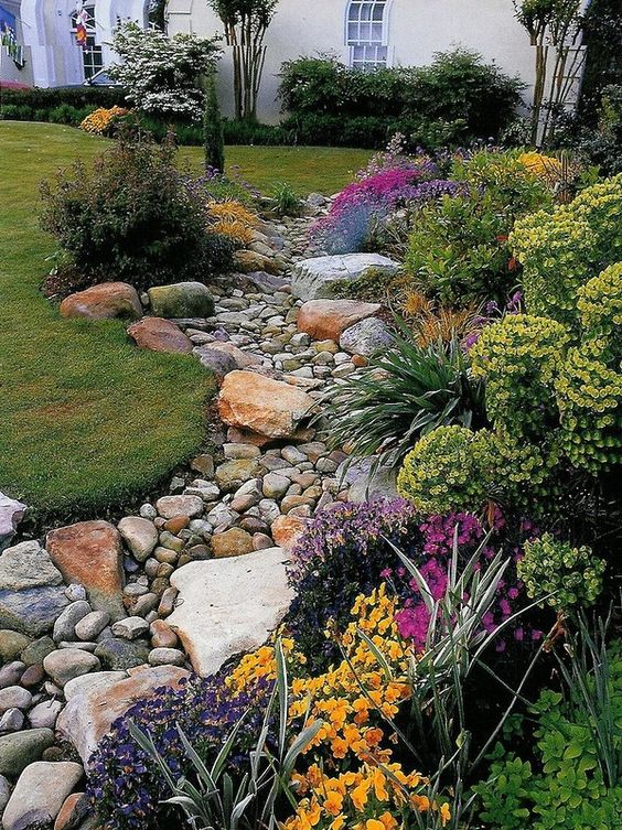 a bright space with rocks and pebbles imitating a river bottom and bright blooms and greenery on the edge is a gorgeous idea