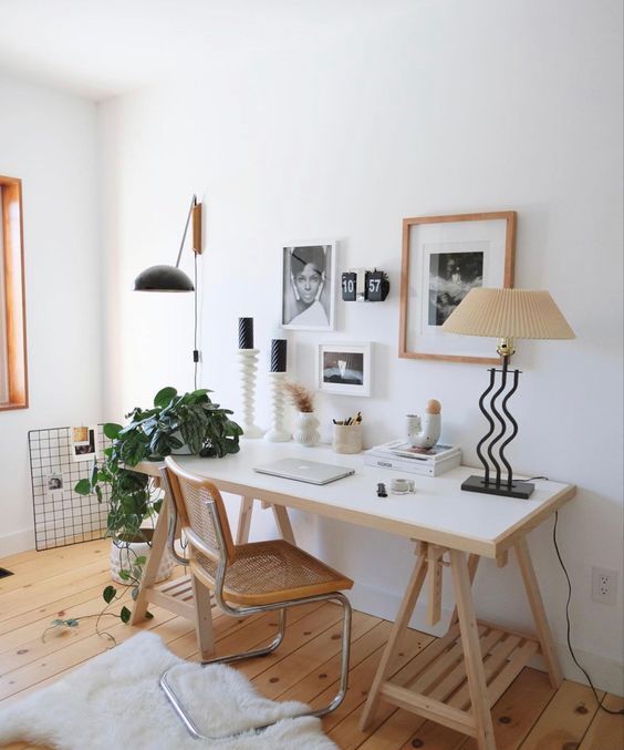 a chic and aesthetic workspace with a trestle desk, a cane chair, some stylsih modern decor, a table lamp and a gallery wall