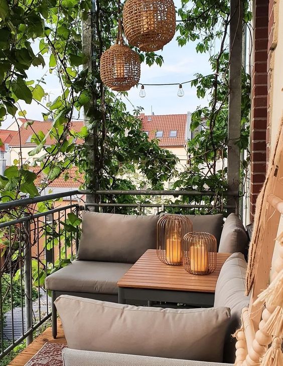 a chic modern balcony with modern furniture, greenery and pendant lamps, candle lantersna dn vines climbin up the whole space