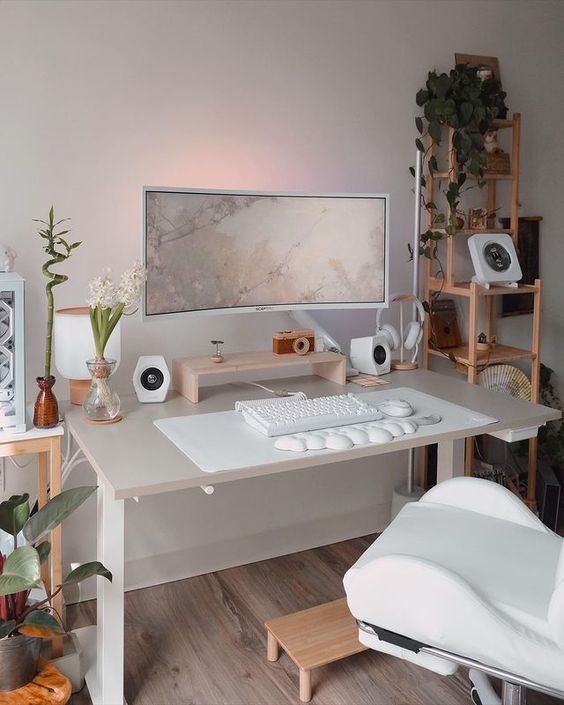 a clean minimal workspace with a desk and a creamy chair, a shelving unit with decor and plants, blooms and greenery