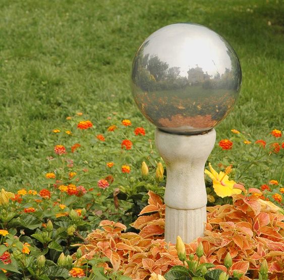 a colorful garden bed with blooms and bright foliage plus a silver garden ball on a stand is a stunning decoration for a garden