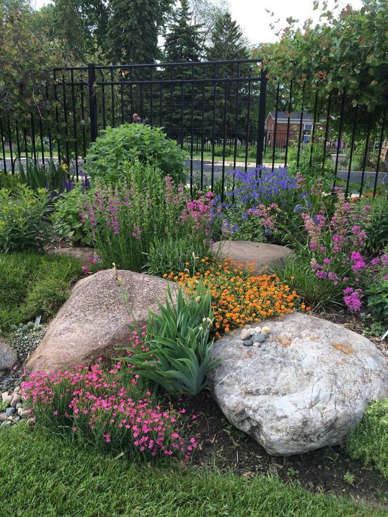 a colorful rock garden with huge rocks, greenery and blooms and a green lawn around is adorable and chic