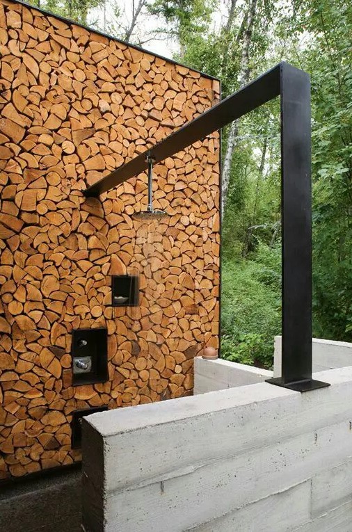 a contemporary rustic outdoor shower with a firewood wall and a dark metal panel