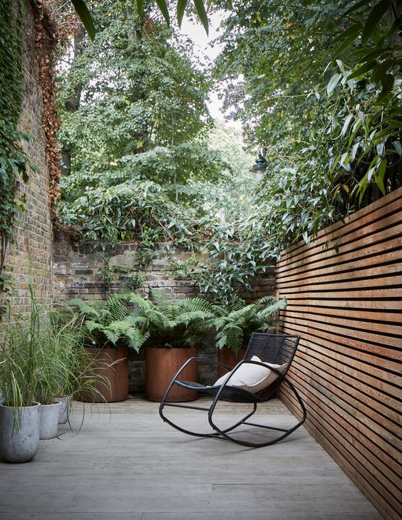 a contemporary side yard with a stained wood and brick fence, potted plants and a black rocker chair