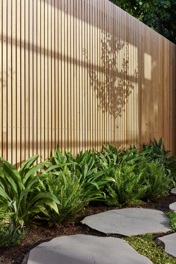 a contemporary space with a light-stained fence, lush greenery along it and a stone path