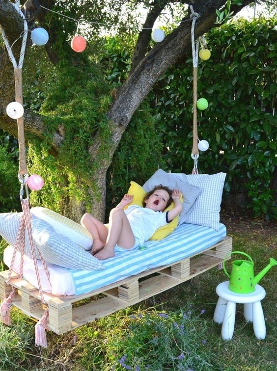 a cool kid pallet daybed hanging on the tree, with colorful lights, pastel bedding and some decor