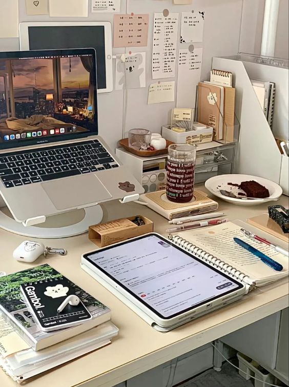 a cool study and workspace with a laptop on a stand, some gadgets, a stand with notebooks, pens and accessories, a gallery wall with memos