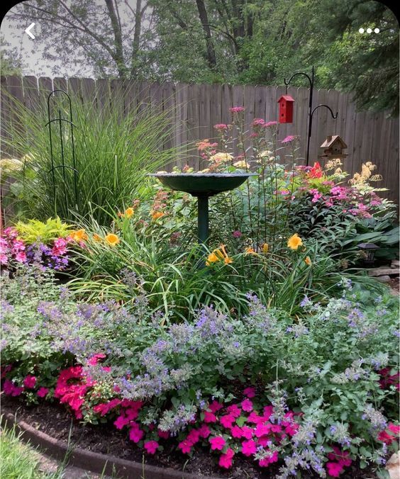 a corner garden as a large flower bed,  with grasses, blooms, a bird bath and some bird houses for attracting them here