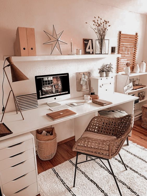 a cozy and aesthetic workspace with a white desk and a shelf, a cane chair, chic decor, a table lamp and some dried blooms for decor