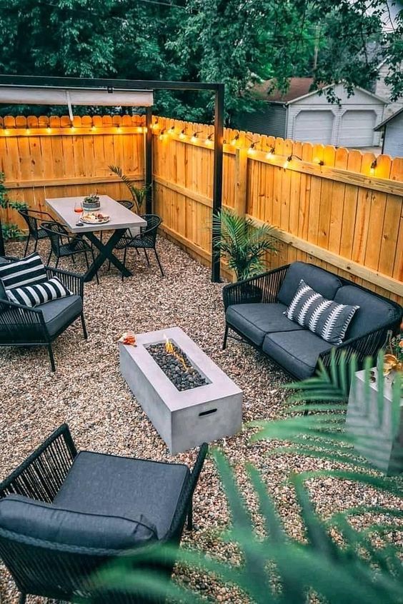 a cozy modern backyard with a stained fence, black and grey seating furniture, a dining set in the corner and a fire pit
