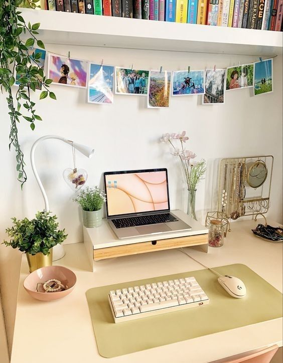 a cozy small workspace with a laptop on a stand, some gadgets and devices, potted plants, a jewelry stand and a banner with pics