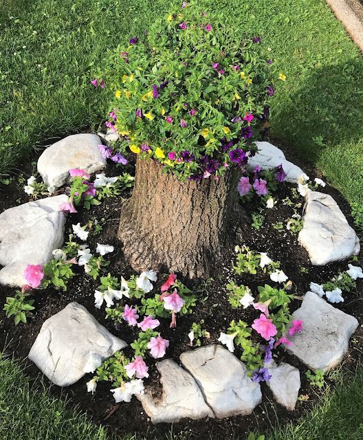 a creative flower bed with rocks, pink and white blooms, a stump with yellow and purple blooms and greenery is a bold decoration