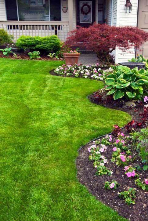A long curved garden bed in the front yard, with greenery and bold blooms plus a green lawn add curb appeal to the house.