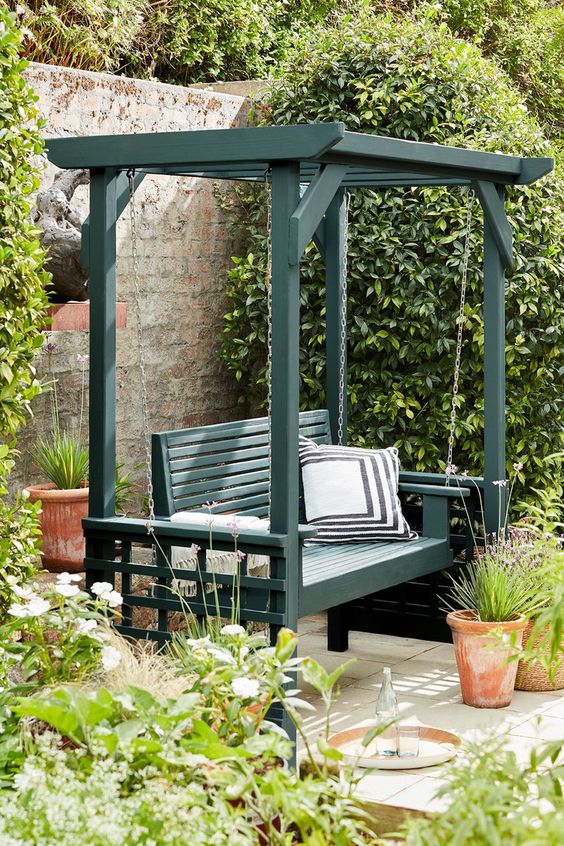 a dark green arbor with a pendant chair and pillows, potted greenery and blooms is a cool idea for a modern outdoor space