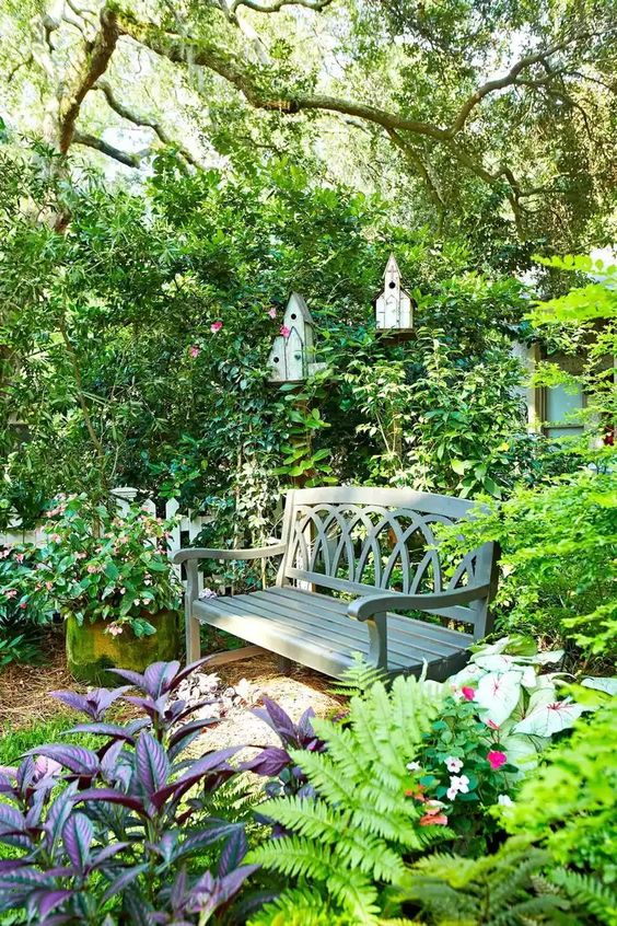 a fab secret garden with lots of greenery and dark foliage around, a dark-stained bench and some bird houses is adorable