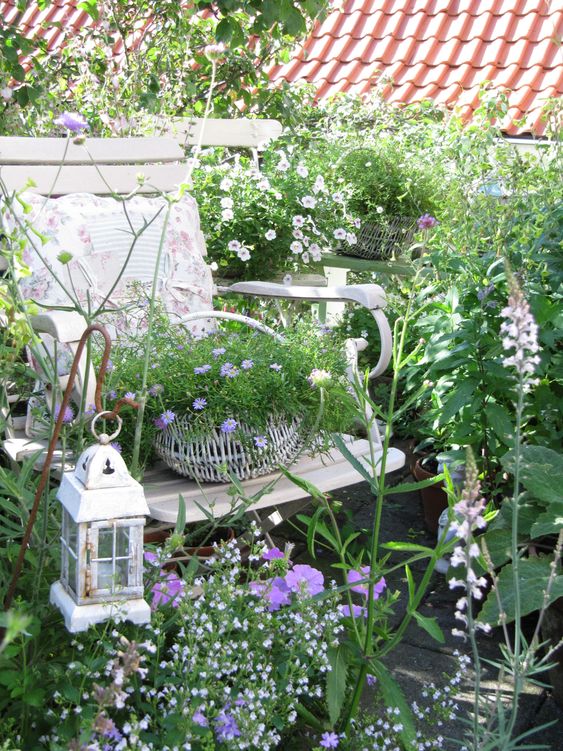 a fairy-tale nook with greenery, white and lilac blooms, a white chair, a basket with blooms and a lantern is stunning