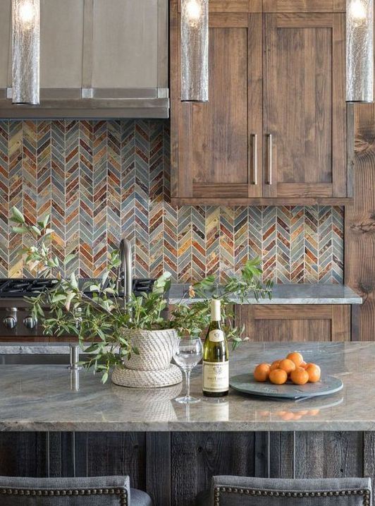 a farmhouse kitchen with stained and dark stained cabinets, stone countertops, a bright chevron tile backsplash and some greenery