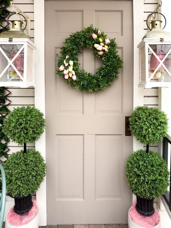 a farmhouse porch with wall lamps with faux tulips, a greenery and tulip wreath and topiaries to line up the front door