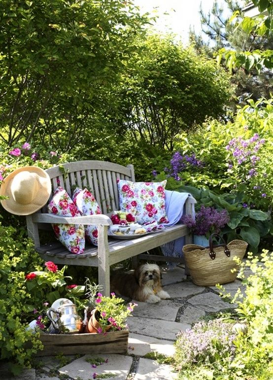 a garden with bushes and blooms, a wooden bench, some crates and blooms, floral pillows is a dreamy space