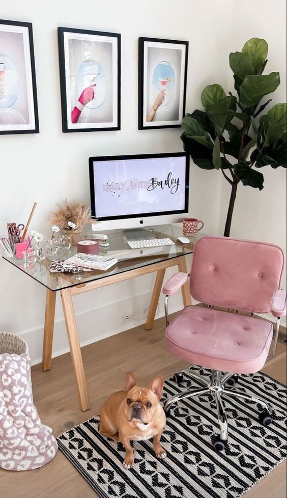 a glam aesthetic workspace with a glass trestle desk, a pink chair, a boho rug, a gallery wall and some decor and a potted plant