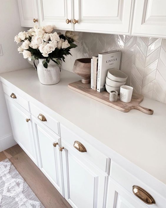 a glam white kitchen with a tan chevron tile backsplash and some chic accessories